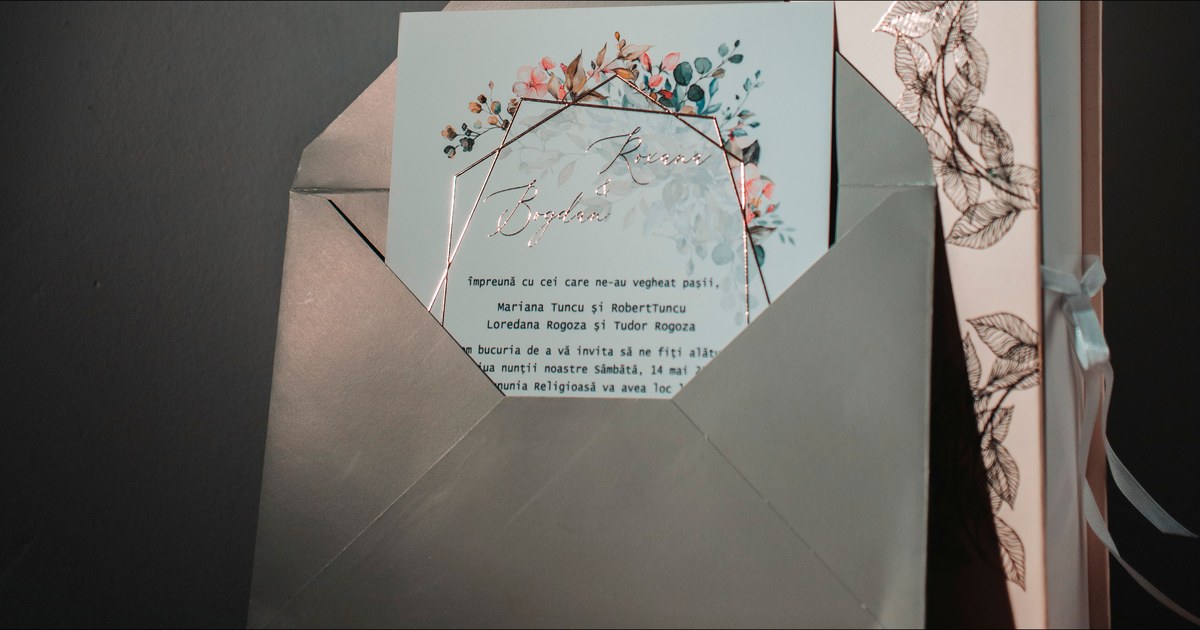 Sage green wedding invitation with a rose gold geometric frame and watercolour florals, tucked into a matching envelope beside a foil-stamped keepsake box, an example of a complete wedding invitation suite