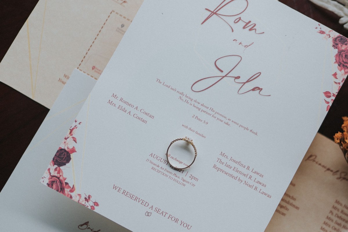 Wedding invitation host line naming both sets of parents alongside the phrase with their families, including a late parent represented by a relative, showing how to word the host line when families are hosting together